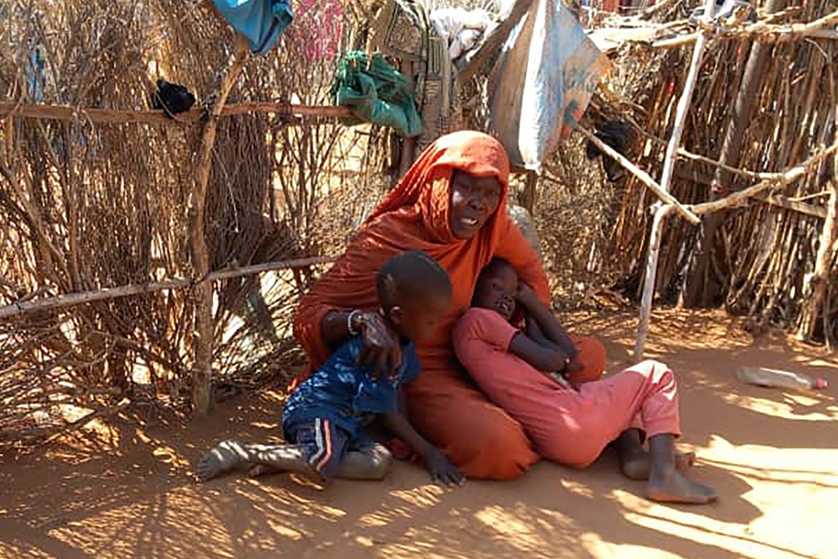 الأم السودانية النازحة منى إبراهيم تجلس مع أطفالها على الأرض في مخيم زمزم للنازحين داخلياً الذي يعاني مجاعة في شمال دارفور (21 ك2 2025، أ ف ب). 